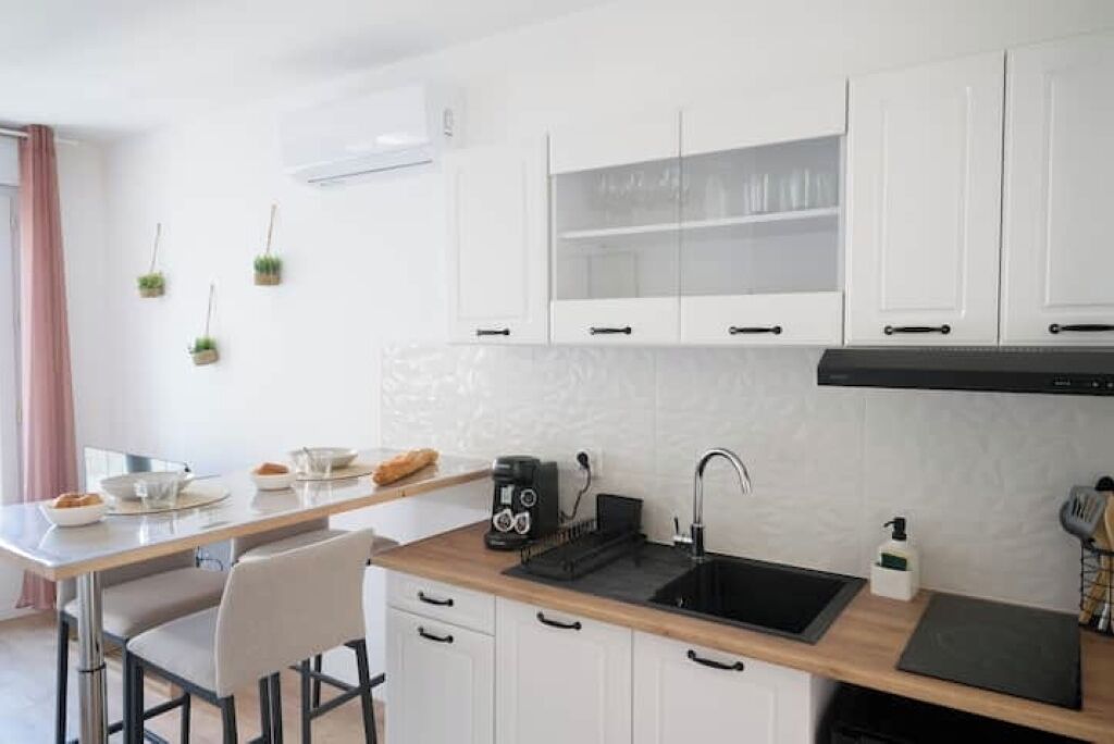 A modern kitchen with white cabinets, a wooden countertop, a black sink, and a coffee maker.