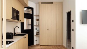 A modern kitchen with a built-in microwave, stove, and black refrigerator. There is a wooden cabinet with a shelf above the sink and a large wooden door with a handle. - Cosy and Modern Apt-jardin de Luxembourg (Paris)