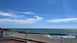 A beach with a clear sky, a rocky shoreline, and a building with a red-tiled roof in the foreground. - Casa Romano SeaFront (Fiumicino)