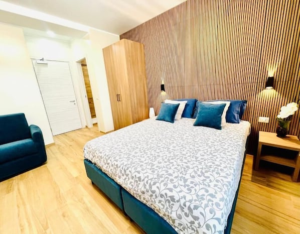 A modern bedroom with a large bed, a wooden wardrobe, and a nightstand with a lamp. - Casa Romano SeaFront (Fiumicino)