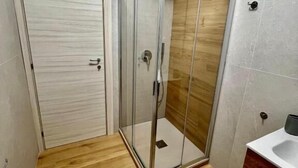 A bathroom with a glass shower enclosure, wooden flooring, a white sink, and a wooden vanity. - Casa Romano SeaFront (Fiumicino)