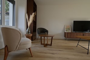 Un salon comprenant un canapé, un fauteuil, une petite table, un téléviseur et une bibliothèque.