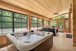 A wooden cabin with a hot tub, large windows, and a ceiling fan.