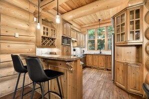 A wooden cabin interior with a kitchen, bar area, and large windows. - Fiddler Lake Resort - Bear 25 (Mille-Isles)