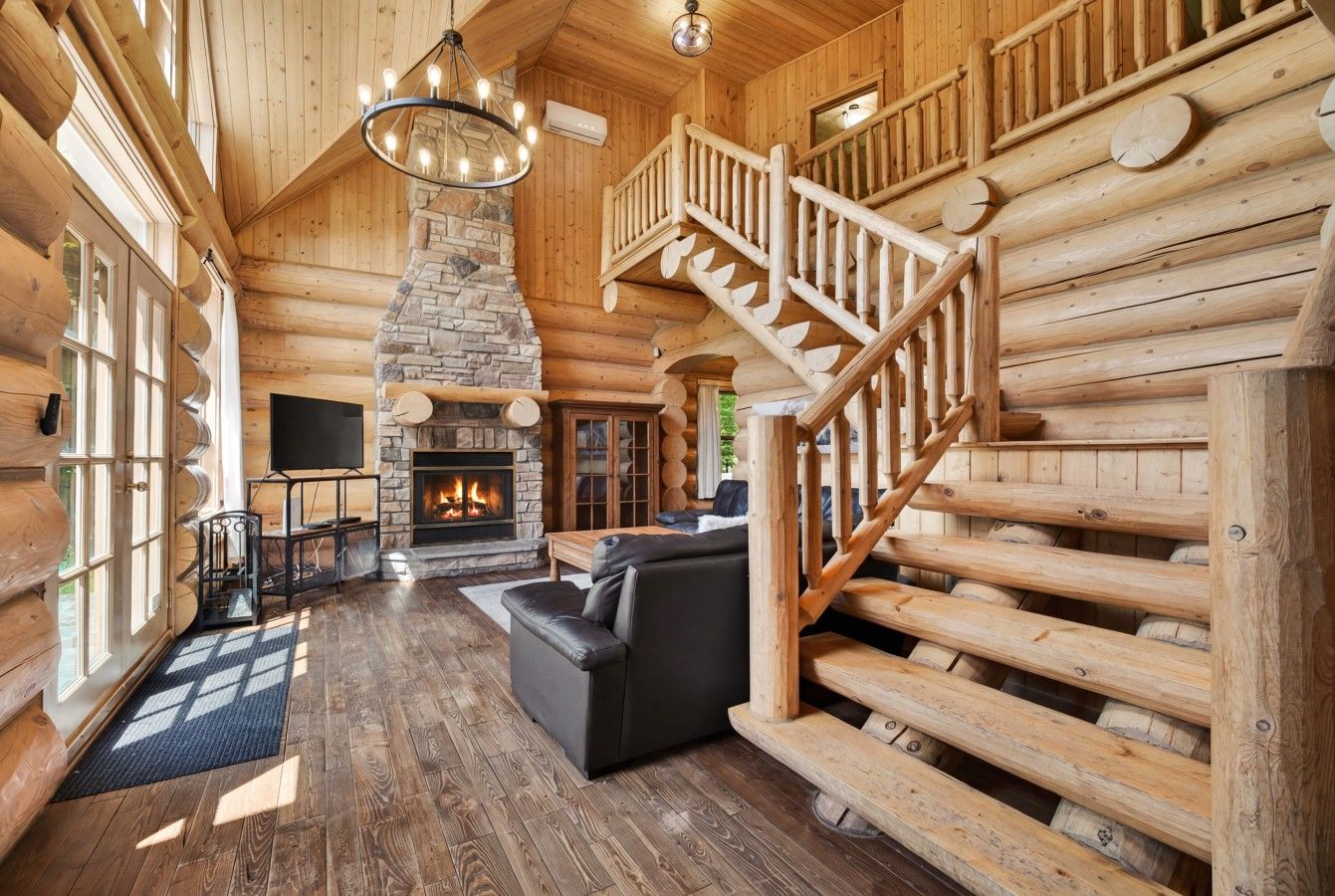 A log cabin interior with a fireplace, a staircase, and a leather sofa.