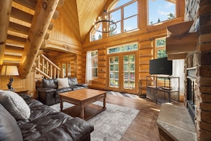 A log cabin interior with a wooden staircase, leather sofa, a coffee table, and a fireplace.