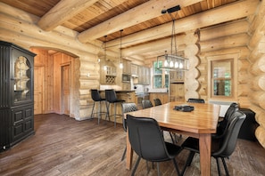 A log cabin interior with a dining area, kitchen, and a large black cabinet.
