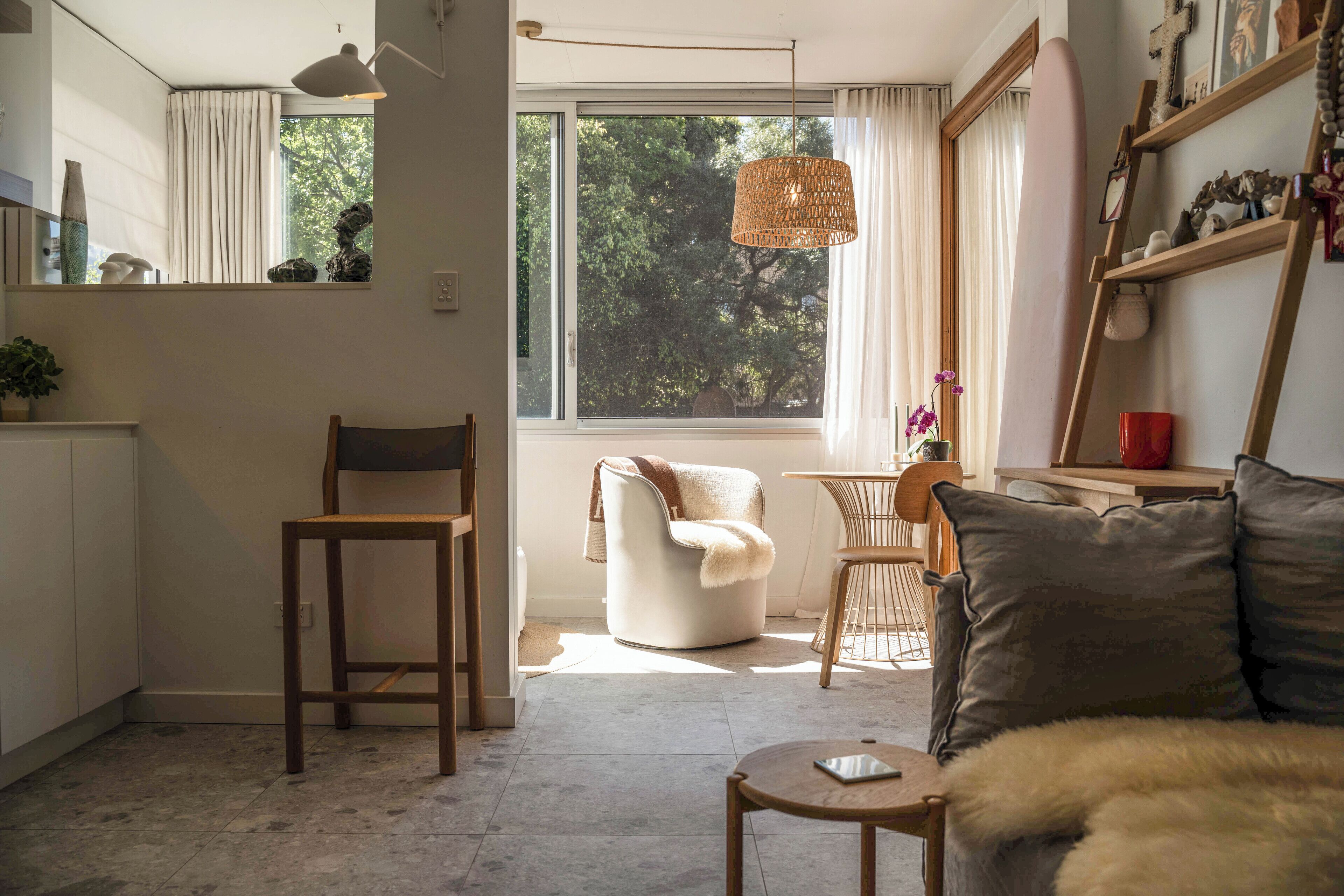 A modern living room with a large window, a sofa, a chair, a small table, and a hanging light fixture.