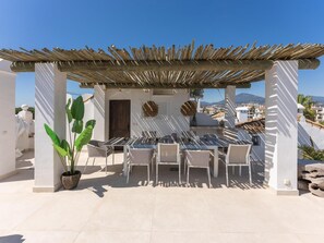Una terraza en la azotea con pérgola, mobiliario exterior y vistas de la ciudad.