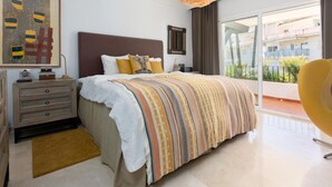 Un dormitorio moderno con una cama grande, una mesita de noche, una lámpara y vistas al balcón exterior.