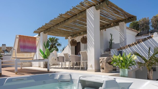 Un área de piscina en la azotea con un jacuzzi, sillones de descanso y una pérgola.