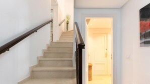 Una escalera con peldaños color beige y barandal negro, que lleva a una habitación con una puerta blanca y un cuadro enmarcado en la pared.
