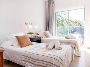 A hotel room with two beds, a nightstand with a lamp, a window with a view of greenery, and a curtain. - Luxurious Villa La Paz Beach Port Aventura Golf (Salou)