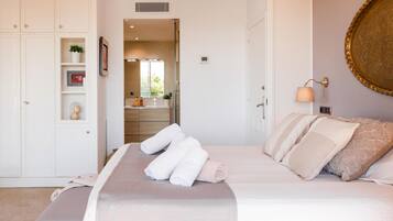 A bedroom with a large bed, a bedside table, a wall-mounted lamp, and a view into the bathroom.