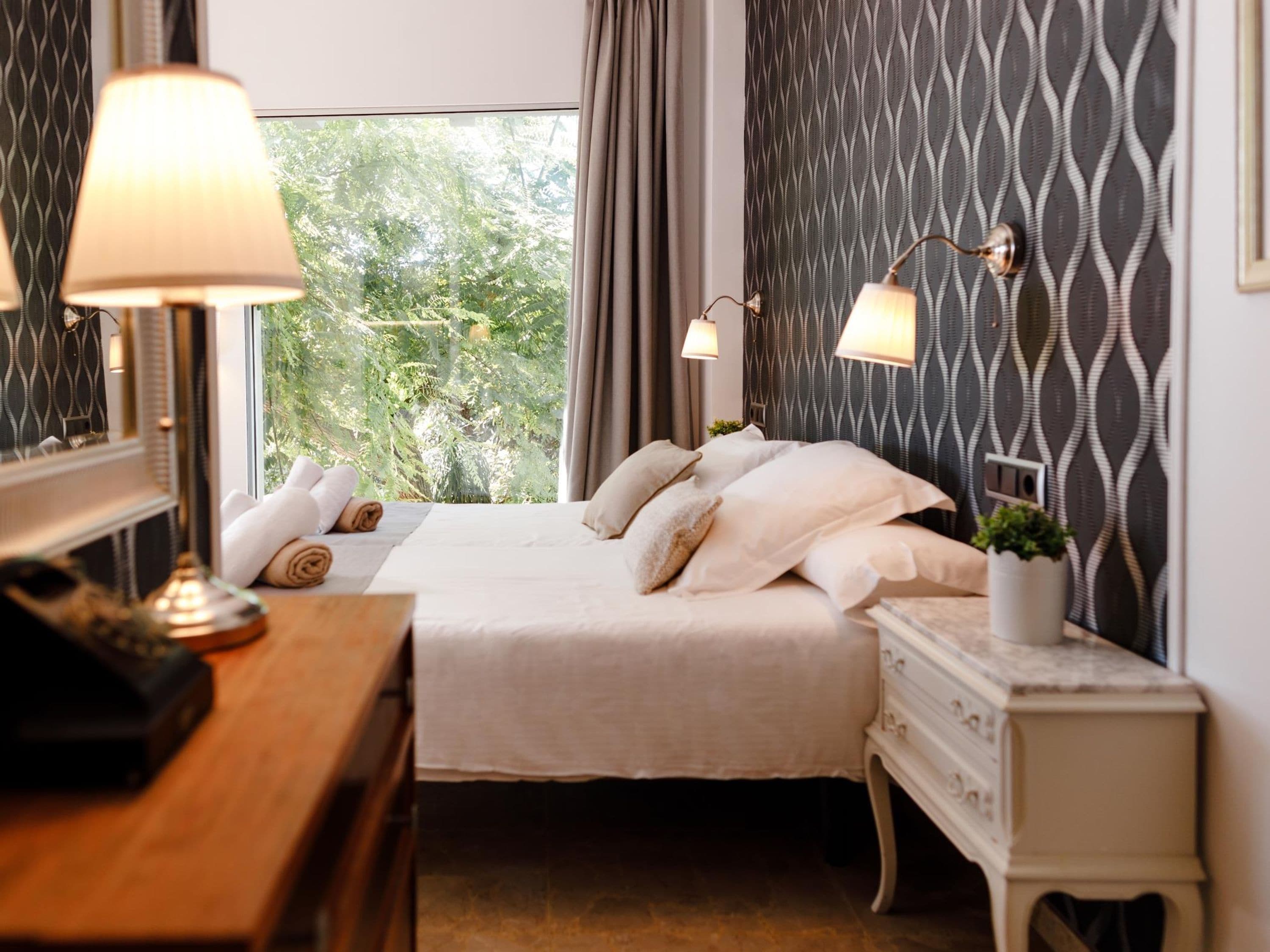 A neatly arranged bedroom with a bed, bedside lamps, a dresser, and a window with curtains.