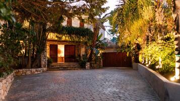 A paved courtyard with a stone wall, a wooden gate, and a building with a stone facade and wooden shutters.
