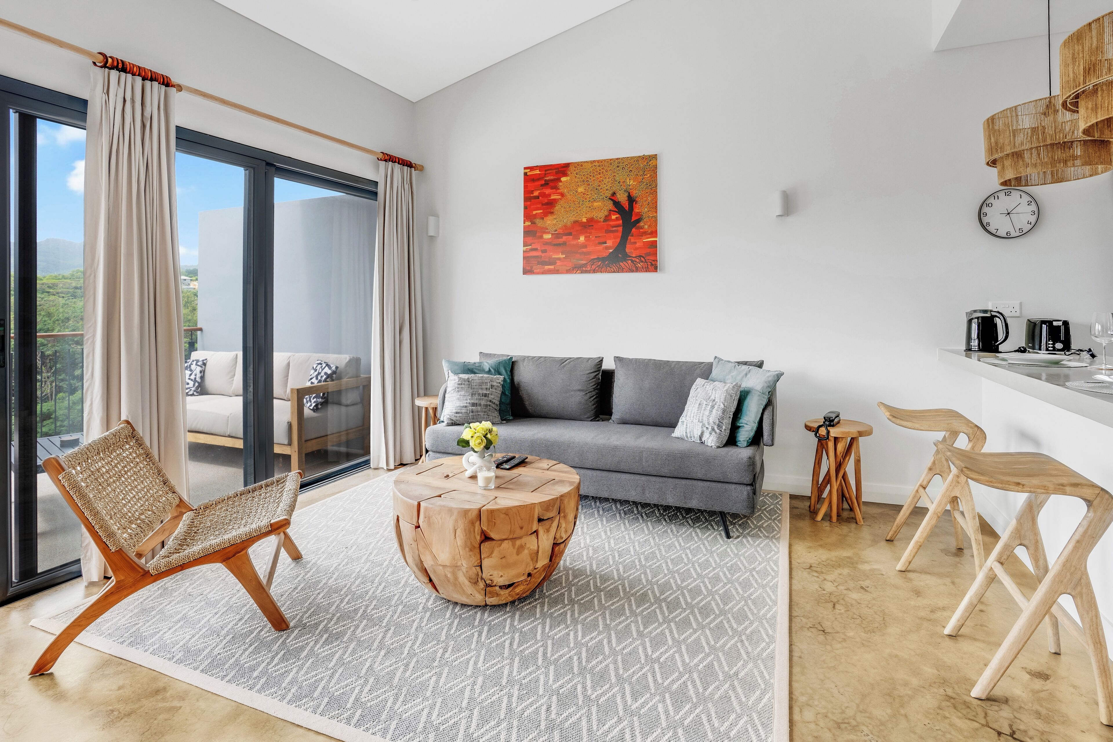 A modern living room with a sofa, a wooden coffee table, a wicker chair, and a dining area with a small table and chairs.