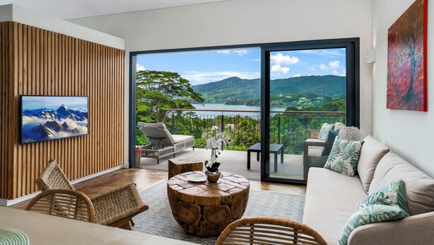 A modern living room with a large TV, comfortable seating, and a scenic balcony view.
