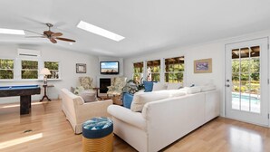 A spacious living room with a pool table, a sofa, and a ceiling fan. - 3 Bedroom Vacation Home with Salt Water Pool (Pawleys Island)