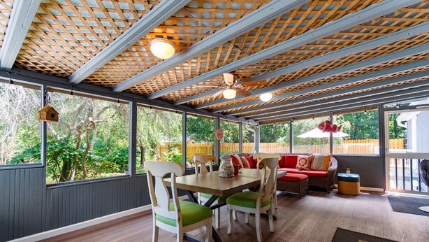A spacious room with a wooden ceiling, large windows, a dining table with chairs, a sofa, and a small rug. - 3 Bedroom Vacation Home with Salt Water Pool (Pawleys Island)