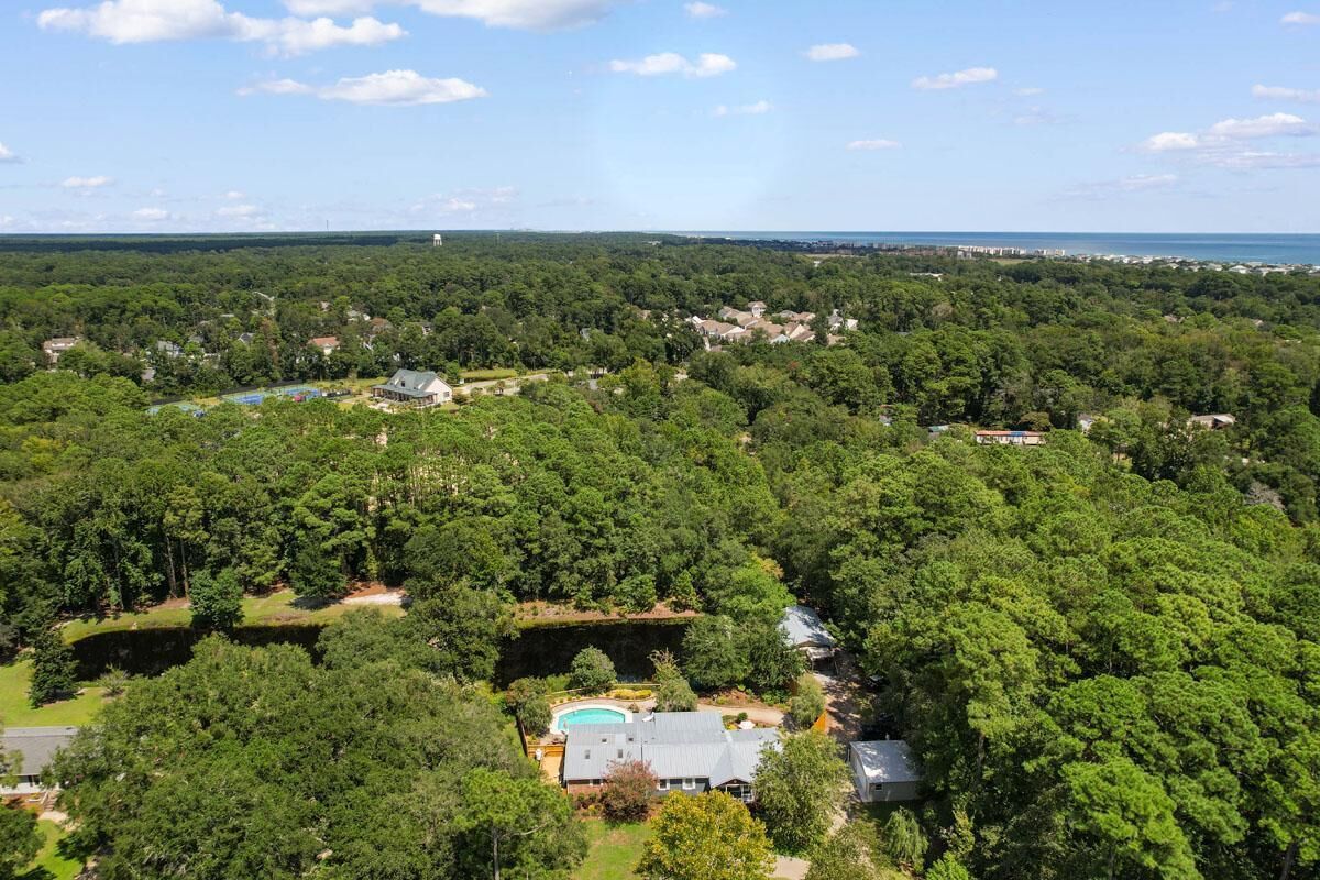 Luchtbeeld van een woongebied met huizen, omringd door weelderige bomen, een zwembad en een vergezicht op de kustlijn.