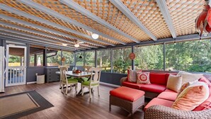 A covered patio area with a dining table and chairs, a red sofa, and wicker furniture. - 3 Bedroom Vacation Home with Salt Water Pool (Pawleys Island)