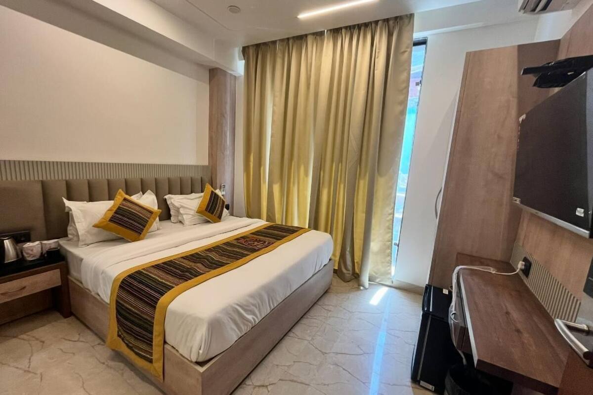 Habitació d'hotel amb un llit gran, una taula de treball, un televisor i una finestra amb cortines.
