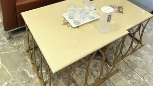 A brown leather sofa, a small table with a white tray holding shot glasses and a white tumbler, and a smartphone on the sofa. - HAVELIYA HOMES BB RESIDENCY (New Delhi)