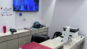 A reception desk with a computer, printer, and a mounted television displaying a security feed.