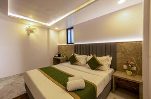 A hotel room with a large bed, a nightstand, a wall-mounted light, and a small window.