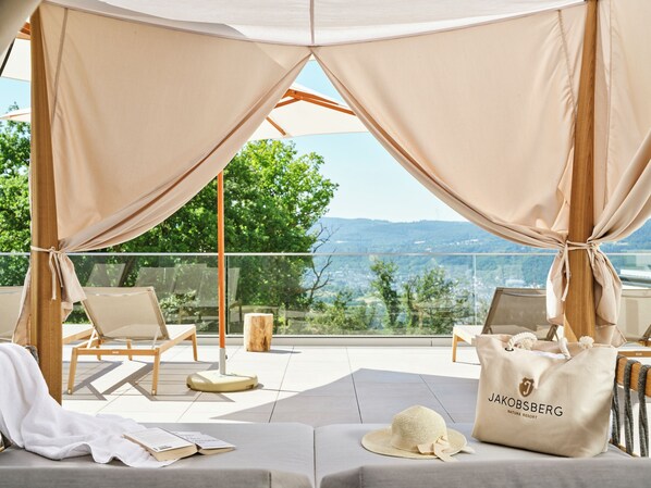 A sunlit outdoor lounge area with a view of the landscape, including trees and hills. - Nature Resort Jakobsberg (Boppard)