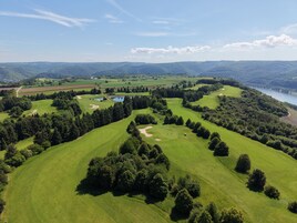 Vista aérea de un campo de golf con múltiples zonas verdes, obstáculos acuáticos y un lago al fondo.
