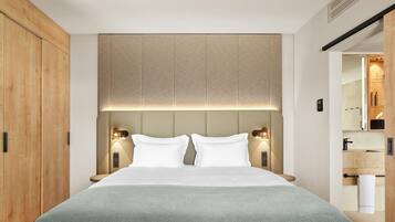 Une chambre d’hôtel moderne avec un grand lit, une armoire en bois et une salle de bain visible à travers une porte ouverte.