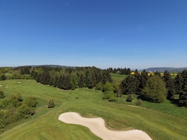Un campo de golf con búnkeres de arena, árboles y un cielo azul despejado.