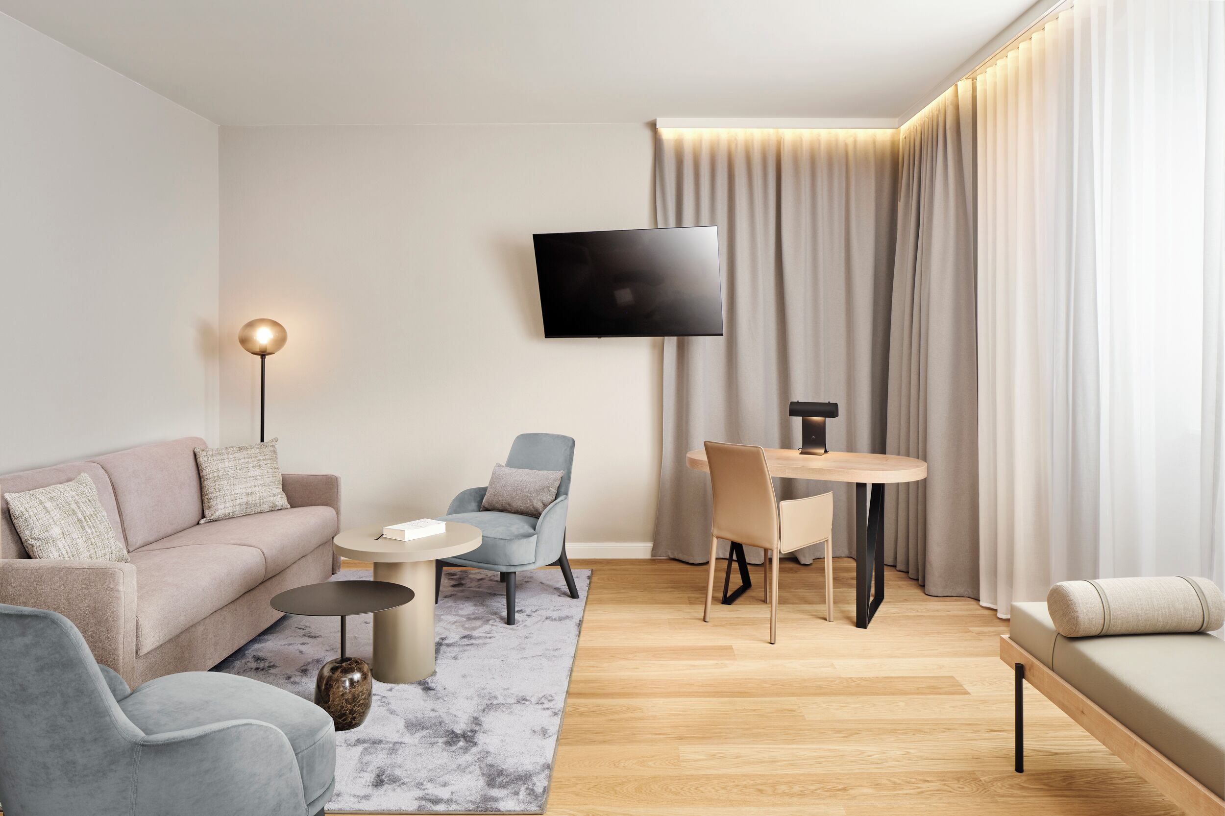 Ein modernes Wohnzimmer mit einer Couch, Sesseln, einem Couchtisch, einem an der Wand montierten Fernseher und einem Essbereich mit Tisch und Stühlen.