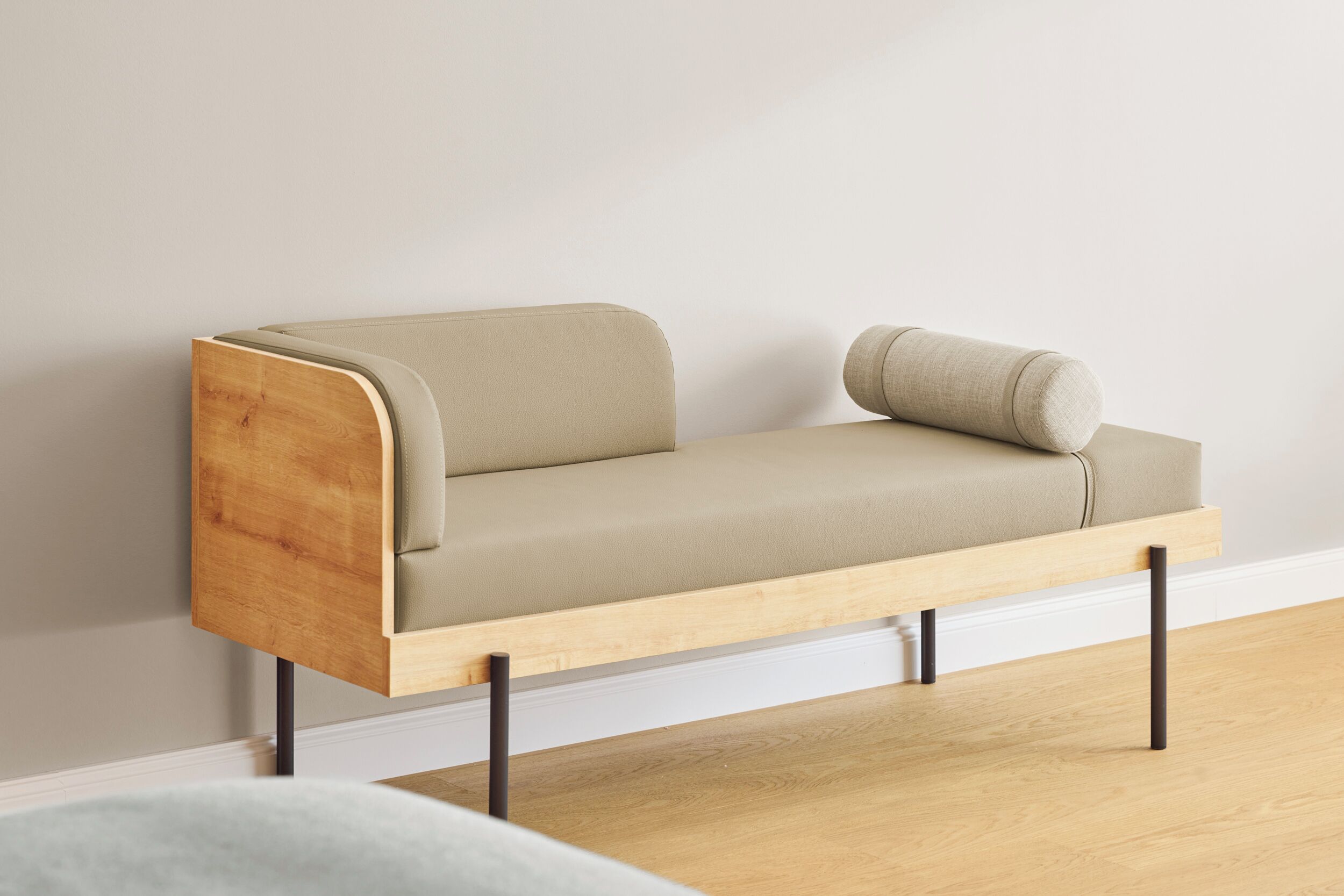 A minimalist sofa with a wooden frame and a light-colored cushion against a plain wall.
