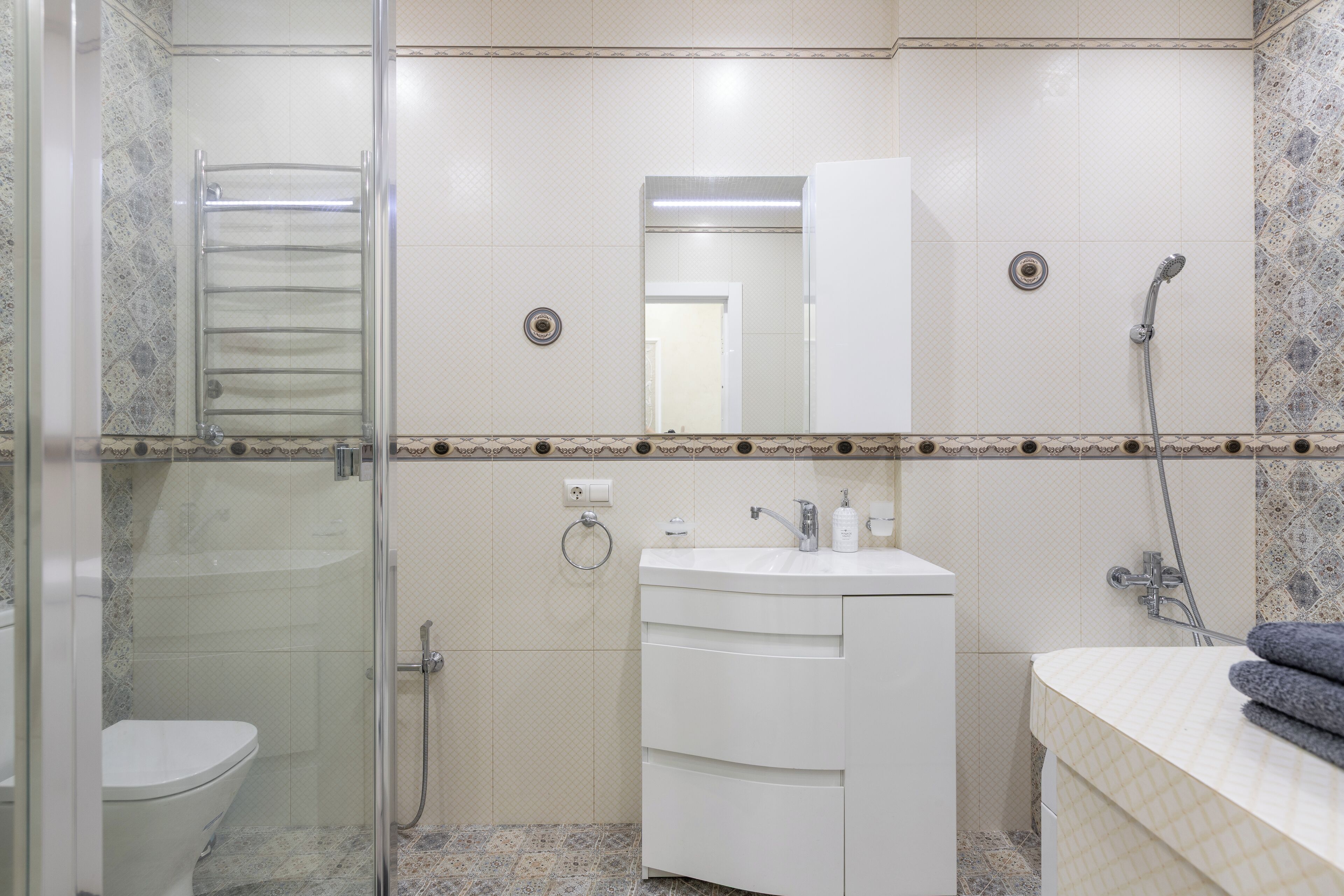 A bathroom with a glass shower enclosure, a toilet, a sink with a mirror, and a towel rack.