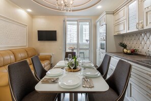 A dining area with a table set for four, surrounded by chairs, a sofa, and a kitchen area with cabinets and a countertop. - Modern apartment with spacious kitchen (Minsk)