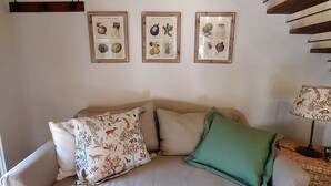 A beige sofa with floral and solid green cushions, a wooden ceiling, and three framed botanical illustrations on the wall. - Casina Laura (Capannori)