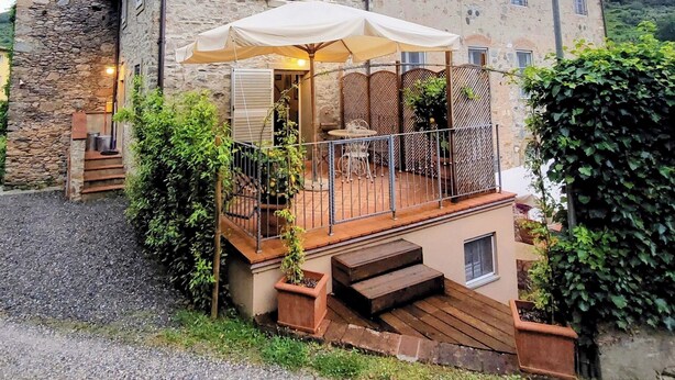 A stone building with a wooden deck, outdoor seating, and a staircase leading to a balcony. - Casina Laura (Capannori)