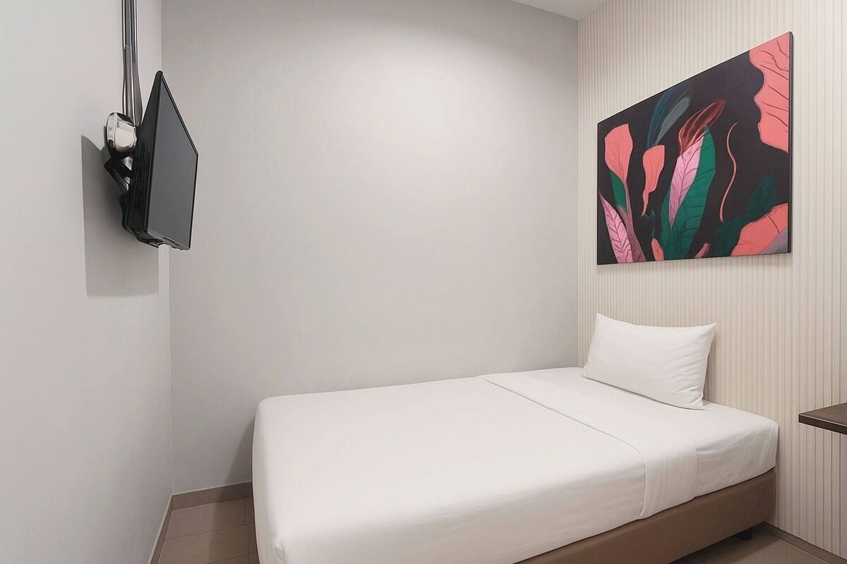 Ein Hotelzimmer mit einem Bett, einem an der Wand befestigten Fernseher und einem farbenfrohen, abstrakten Gemälde über dem Bett.