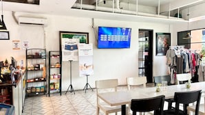 Una habitación con televisor grande, una mesa, sillas, un perchero y una estantería con aperitivos.