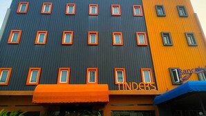 Un edificio de varios pisos con una combinación de fachadas oscuras y claras, que presenta un letrero llamativo que dice 'Rancak Tinders'.