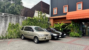 Un estacionamiento con dos autos, un edificio con detalles naranja y una cerca con follaje.