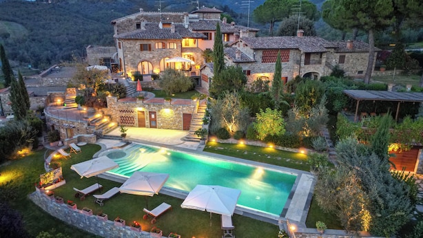 Un edificio grande de piedra con piscina, mobiliario exterior y un jardín bien iluminado.