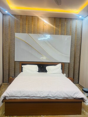 A modern bedroom with a large bed, a ceiling light, and a wall-mounted TV. - Shri Radhika Dham (Mathura)