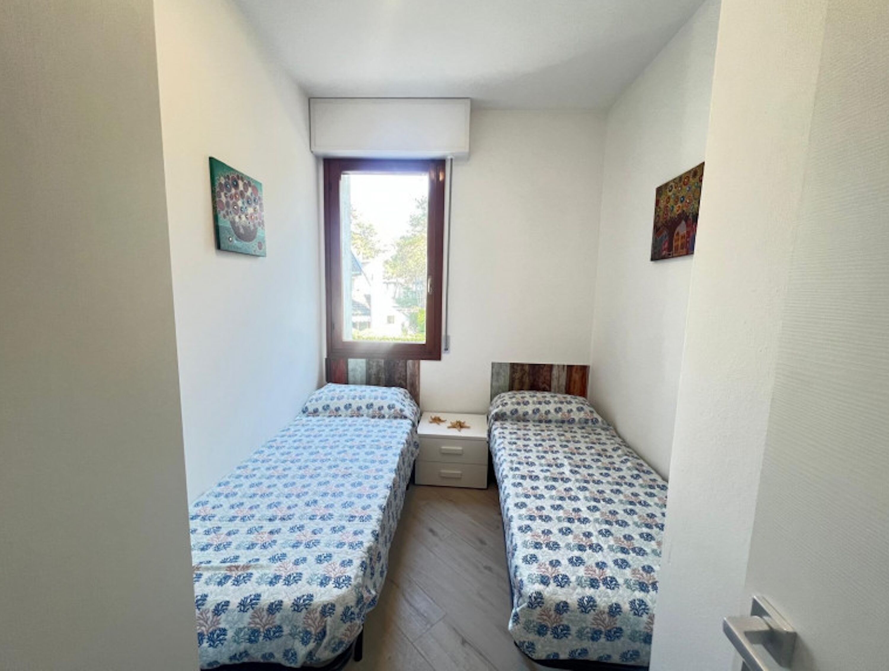 Una stanza piccola e stretta con due letti singoli, una finestra e una porta.