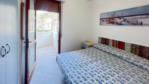 A bedroom with a bed, a painting on the wall, and a door leading to an outdoor area.
