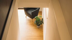 Un escalier en bois mène à une pièce où se trouvent une chaise noire, une plante en pot et un objet décoratif en forme d’ananas.