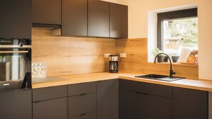 Une cuisine moderne avec des meubles de couleur sombre, un plan de travail en bois, une machine à café et une fenêtre donnant sur un paysage verdoyant.